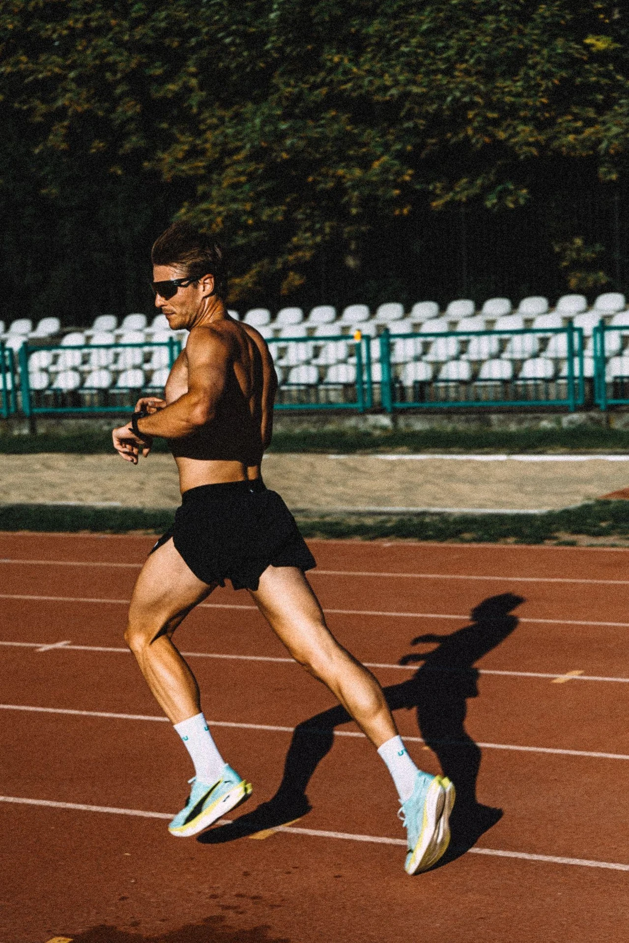 Mężczyzna chce dokonać niemożliwego Biegacz w ciemnych okularach i sportowym stroju biegnie po tartanowej bieżni, spoglądając na zegarek podczas intensywnego treningu.
