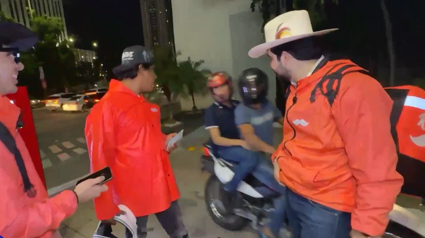 Tragedia podczas transmisji na żywo. Popularny influencer nie żyje Grupa osób w pomarańczowych kurtkach i dwie osoby na motocyklu na nocnej ulicy.