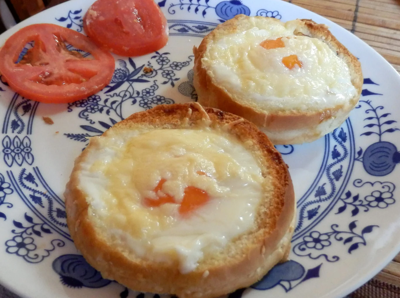 Grzanki z jajkami doskonale sprawdzą się na śniadanie, a także kolację lun lunch Dwie grzanki z jajkiem i serem oraz dwa plastry pomidora na ozdobnym talerzu.