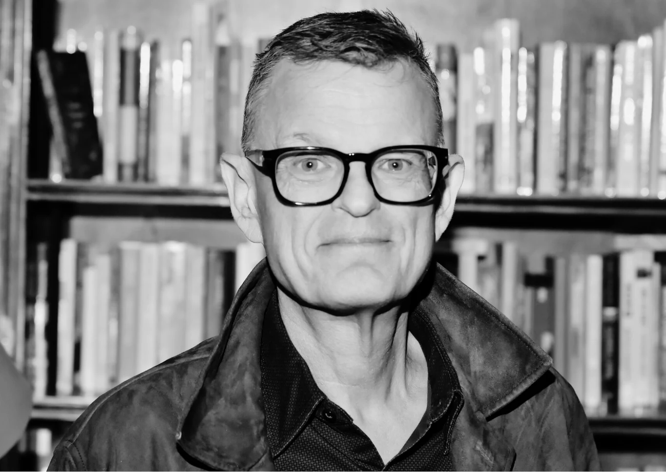 Andrzej Morozowski Mężczyzna w okularach i kurtce stoi na tle półek z książkami.