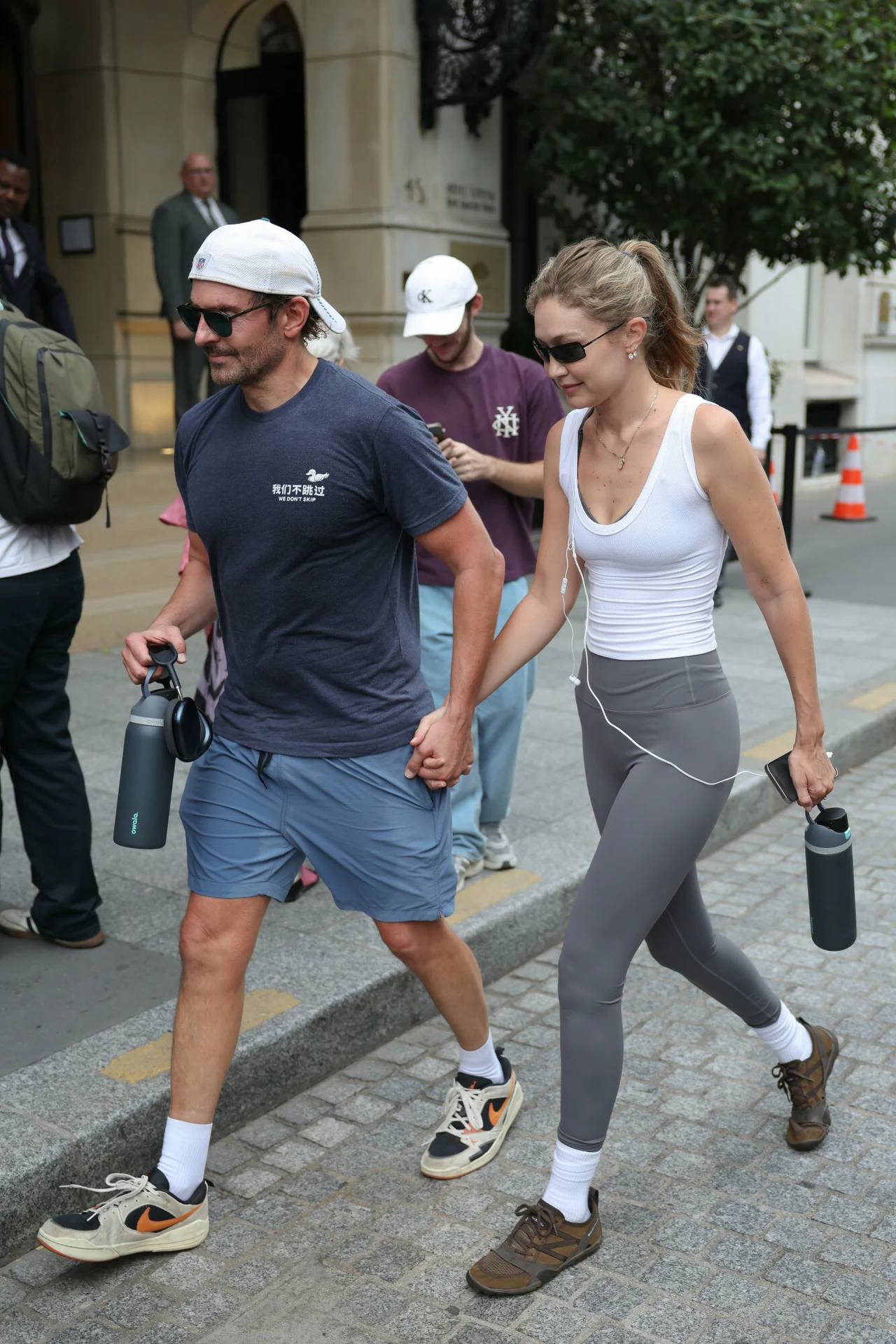 Gigi Hadid i Bradley Cooper w Paryżu. Para wzięła sekretny ślub? Para trzymająca się za ręce podczas spaceru, ubrana sportowo, oboje mają okulary przeciwsłoneczne i butelki na wodę, idą chodnikiem miejskim.
