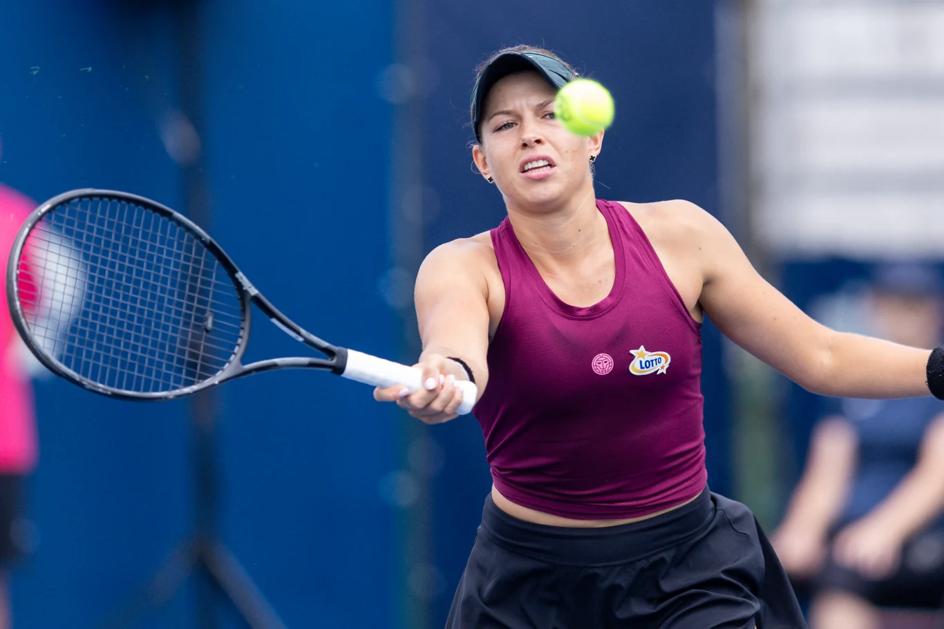 Weronika Falkowska Kobieta w bordowej koszulce i czapce sportowej odbijająca piłkę tenisową rakietą podczas meczu.
