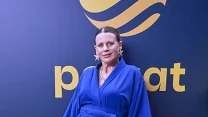 Kobieta w niebieskiej sukni i dopasowanych kozakach pozująca na czerwonym dywanie na tle ścianki z charakterystycznym żółtym logo Polsatu.