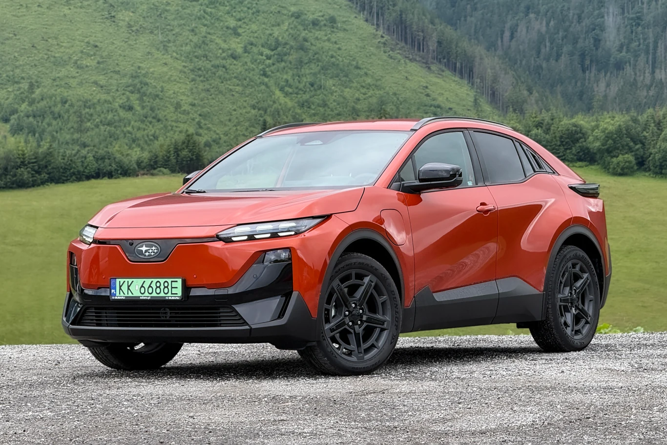 Uncharted to pierwszy kompaktowy SUV Subaru z napędem elektrycznym. Czerwony elektryczny SUV Subaru Uncharted z czarnymi felgami, zaparkowany na tle zielonych wzgórz