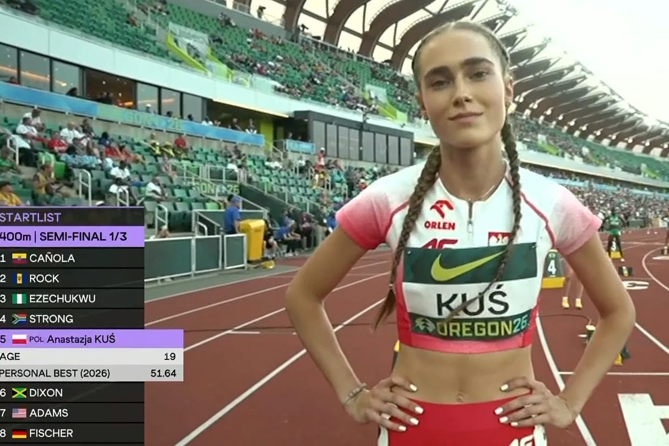 Anastazja Kuś przed półfinałem w Eugene Lekkoatletka w biało-czerwonym stroju z napisem 'Kuś' oraz numerem startowym stoi na stadionie lekkoatletycznym, z relacją z biegu na 400 metrów na tle trybun oraz ekranu z listą startową i rekordem życiowym 51,64.