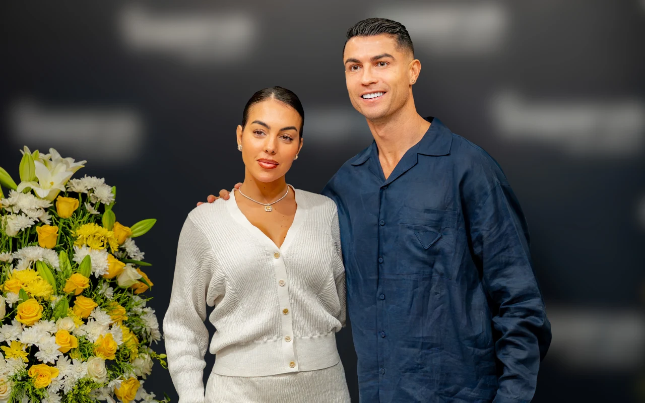 Georgina Rodriguez i Cristiano Ronaldo Dwie elegancko ubrane osoby stojące obok siebie, jedna z nich z dłonią na ramieniu drugiej, w tle duży bukiet białych i żółtych kwiatów.