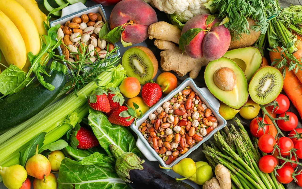Jak działa dieta wegańska? Naukowcy zajrzeli głębiej niż zwykle Różnorodne świeże owoce i warzywa, takie jak banany, truskawki, brzoskwinie, awokado, kalafior, marchew, pomidory, cukinia, szparagi oraz mieszanka orzechów i fasoli w miseczkach.