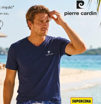 Męski T-shirt Pierre Cardin za 34,99 zł. Mężczyzna w granatowej koszulce z logo Pierre Cardin, stojący na plaży z jasnym piaskiem i błękitnym morzem w tle.