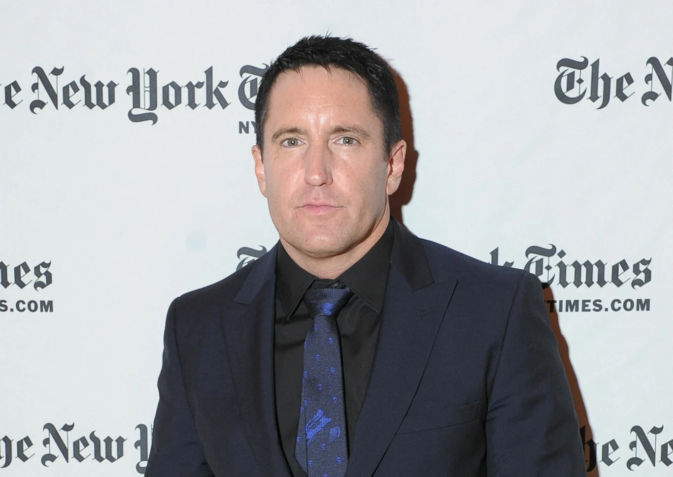 Trent Reznor Trent Reznor w ciemnym garniturze, czarnej koszuli i granatowym krawacie na tle logo The New York Times.