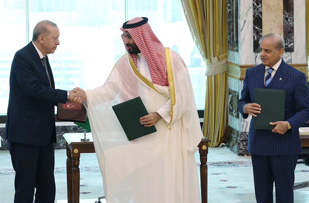 Turcja, Arabia Saudyjska i Pakistan zawarły sojusz. Na zdj. przywódcy wymienionych państw Przywódcy Turcji, Arabii Saudyjskiej i Pakistanu w eleganckich strojach, dwóch podaje sobie dłonie, wszyscy z dokumentami.
