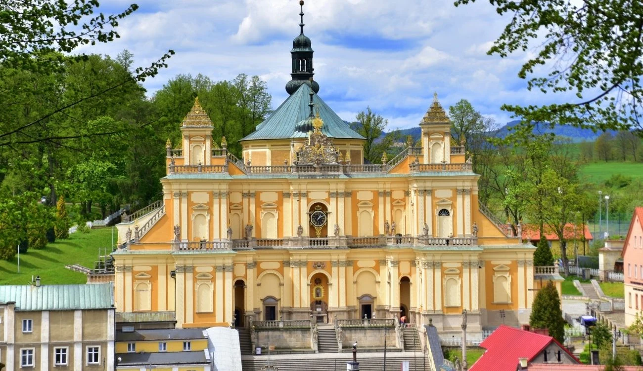 Bazylika w Wambierzycach - cel pielgrzymów i atrakcja turystyczna Bazylika w Wambierzycach z kopułą i wieżyczkami, otoczona zielenią i budynkami w pobliżu.