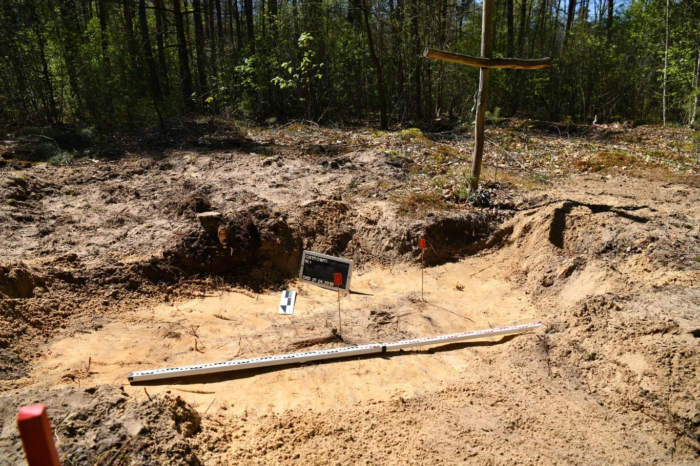 IPN poinformował o zakończeniu prac ekshumacyjnych w Ostrówkach i Woli Ostrowieckiej na Wołyniu Wykop archeologiczny IPN w Ostrówkach, krzyż, oznaczenie miejsca badań, narzędzia pomiarowe na piasku.