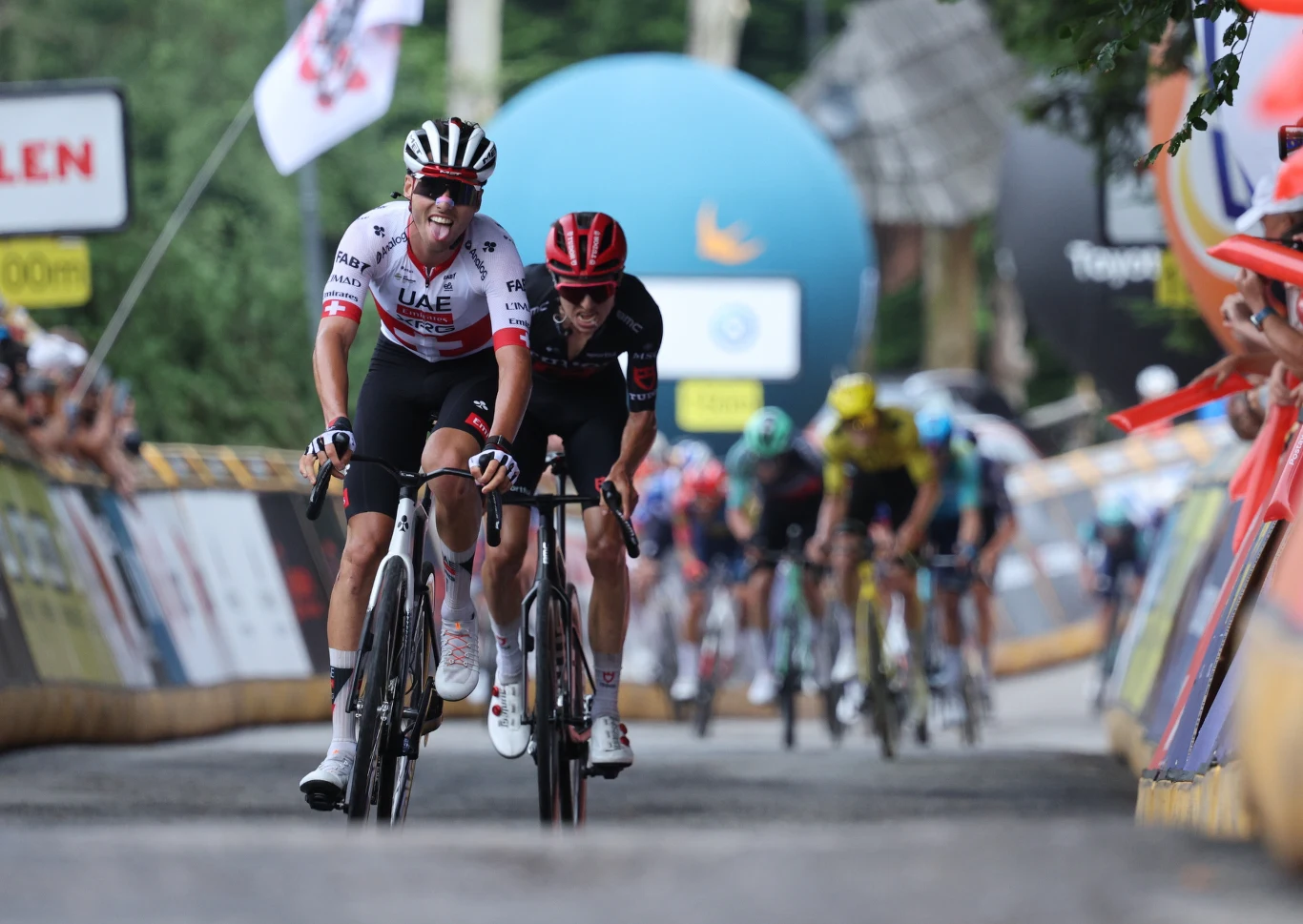 Jan Christen oraz jadący tuż za nim Marco Brenner Jan Christen przed Marco Brennerem podczas podjazdu, za nimi peleton kolarzy w różnokolorowych koszulkach.
