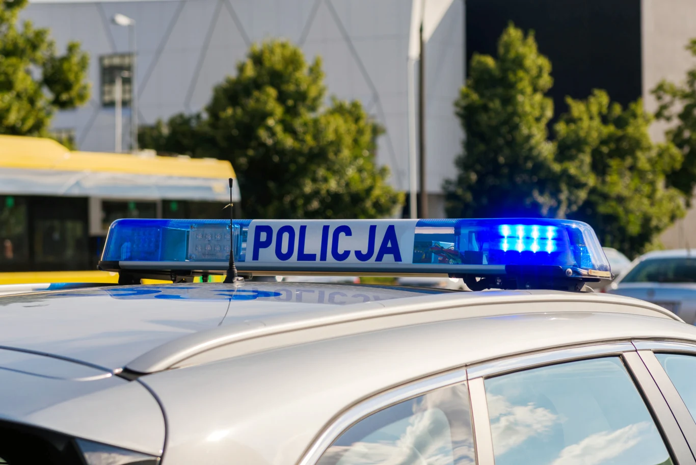 Policja poszukiwała trzech sióstr. Szczęśliwy finał (zdj. ilustracyjne) Sygnalizator świetlny na radiowozie policyjnym; w tle żółty tramwaj oraz biały budynek.