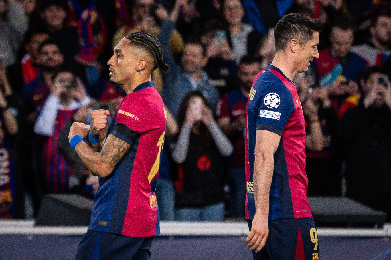 Raphinha i Robert Lewandowski Raphinha i Robert Lewandowski w koszulkach FC Barcelony na boisku. W tle widoczni kibice na trybunach.