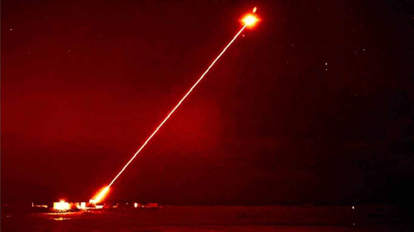 Amerykańska armia szykują się na przyjęcie laserów bojowych do niszczenia dronów (zdjęcie ilustracyjne). Wiązka czerwonego lasera skierowana z ziemi w niebo, jasny rozbłysk na końcu wiązki, ilustracja systemu antydronowego.