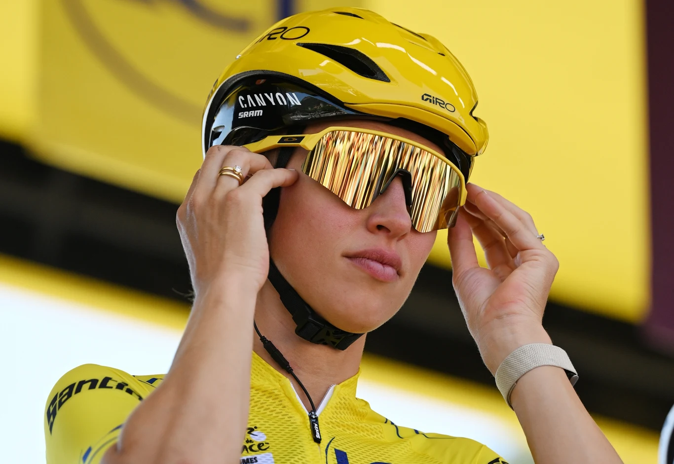 Katarzyna Niewiadoma-Phinney Kolarz w żółtym stroju i kasku, poprawiający sportowe okulary przeciwsłoneczne, skoncentrowany przed startem wyścigu.