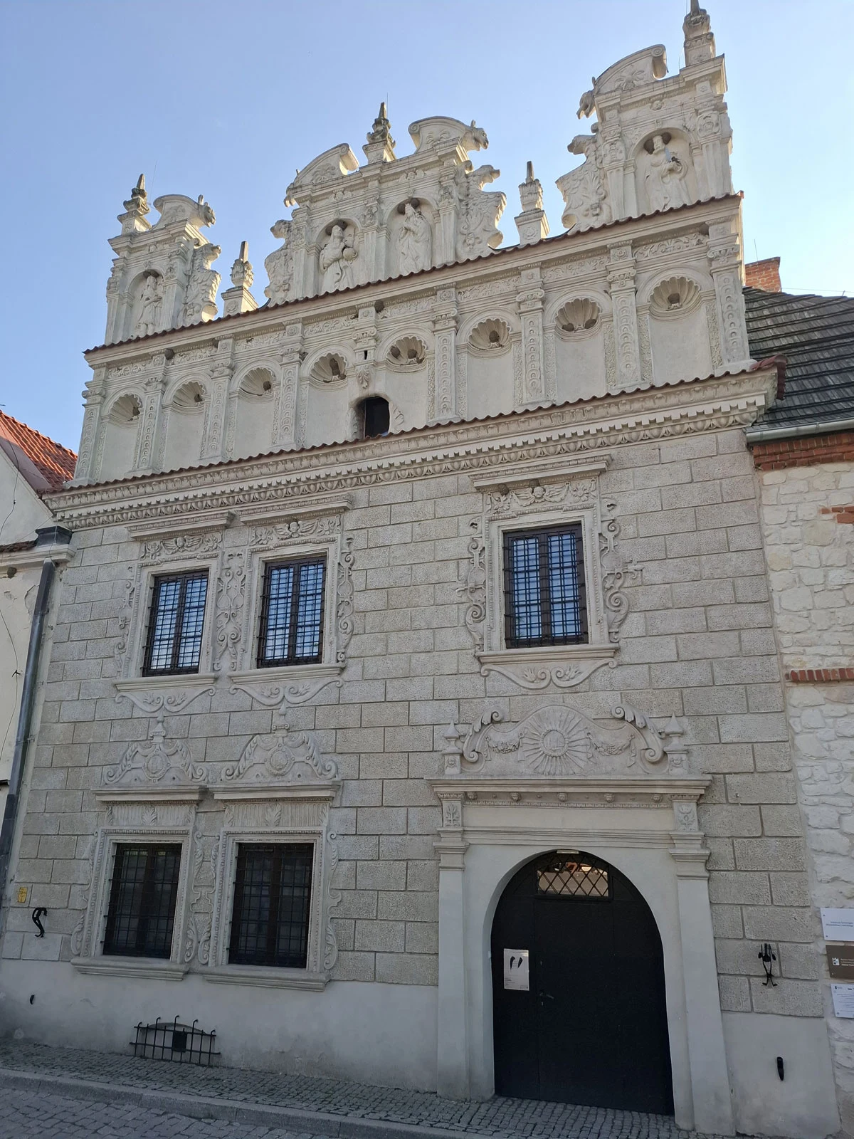 Renesansowa kamienica z bogato zdobioną attyką i prostokątnymi oknami, ozdobiona reliefami oraz detalami architektonicznymi wokół drzwi i okien.