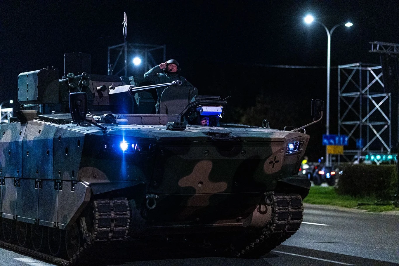 BWP Borsuk podczas przygotowań do defilady z okazji Święta Wojska Polskiego 2026 roku. Opancerzony pojazd wojskowy jedzie ulicą nocą, żołnierz salutuje stojąc w odkrytym włazie, pojazd oświetlają niebieskie reflektory.