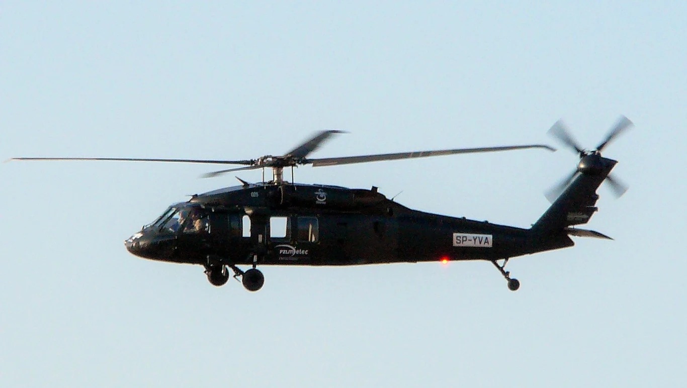 S-70i Black Hawk w locie. Czarny śmigłowiec wojskowy typu Black Hawk w locie na tle jasnego nieba.