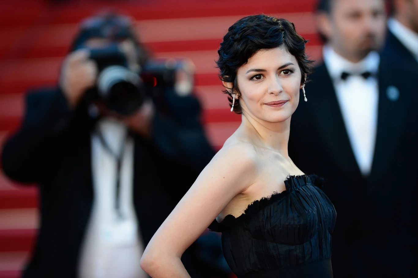 Audrey Tautou na festiwalu filmowym w Cannes Audrey Tautou na czerwonym dywanie w Cannes, w czarnej sukni, z krótkimi włosami; w tle fotograf z aparatem.