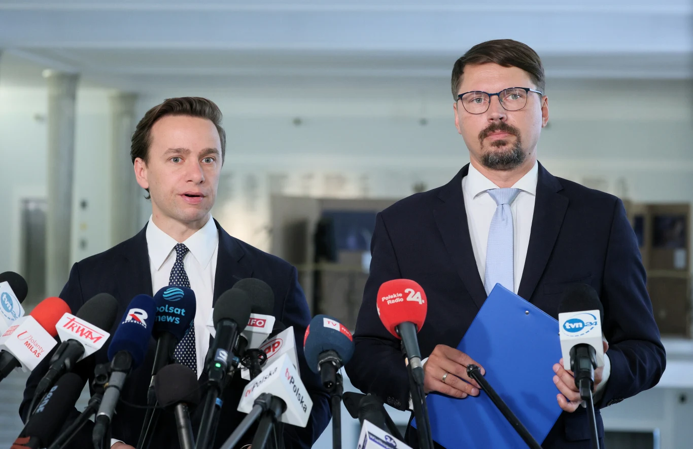 Konfederacja chce wyrzucić do kosza polski system kaucyjny Dwóch mężczyzn w garniturach przed mikrofonami, jeden trzyma niebieską teczkę i notes podczas konferencji Konfederacji.