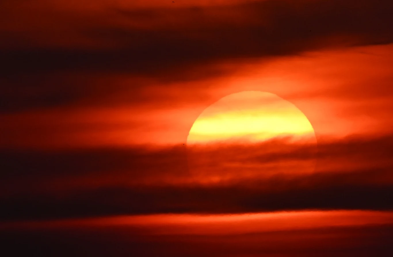 Katastrofalne skutki zmiany klimatu są już odczuwalne w Europie Częściowo zasłonięte słońce za ciemnymi chmurami, czerwono-pomarańczowe niebo nad Europą.