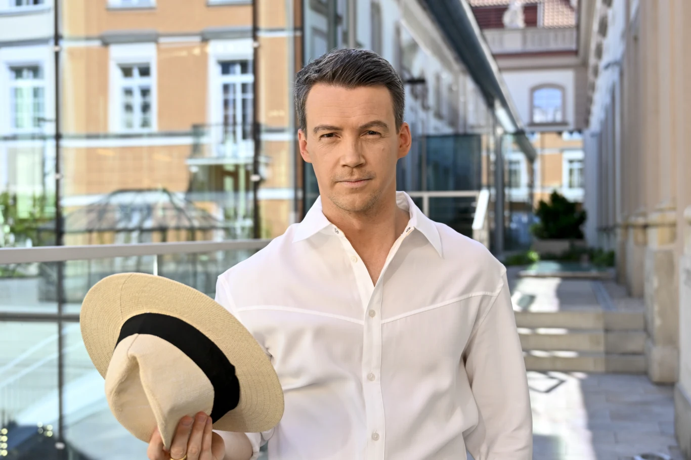 Krzysztof Kwiatkowski Krzysztof Kwiatkowski w białej koszuli i z kapeluszem w ręku na tle budynków podczas przygotowań do Tańca z gwiazdami