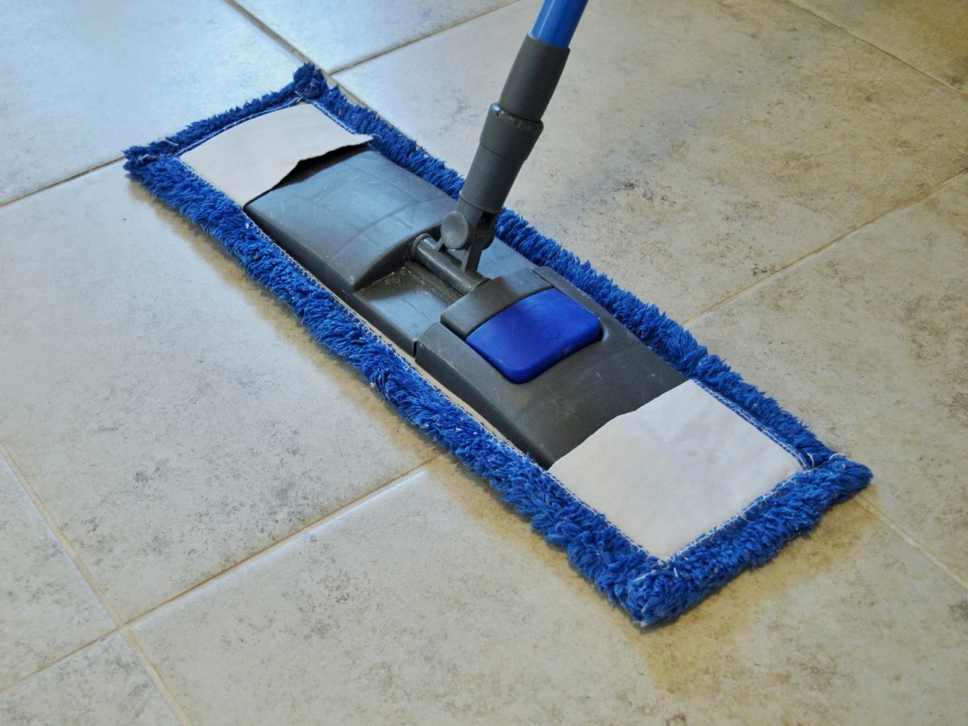 Jak zdezynfekować podłogę w łazience domowym sposobem? Płaski mop z niebieskim obramowaniem podczas mycia jasnych, ceramicznych płytek w łazience.