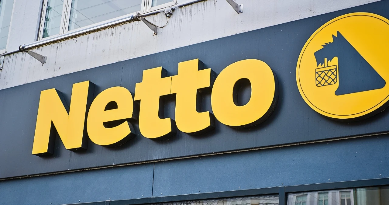 Jak uporządkować szafę za mniej niż 100 zł? Netto ma organizery od 9 zł Wejście do sklepu Netto z żółtym logo i grafiką psa z koszykiem na tle ciemnoniebieskiej tablicy.