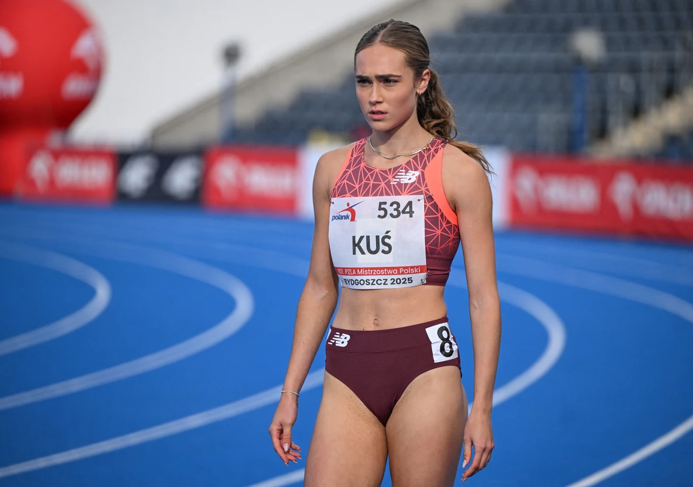 Anastazja Kuś Lekkoatletka w sportowym stroju, z numerem startowym 534, stoi na niebieskiej bieżni przed rozpoczęciem biegu, skupiona i gotowa do rywalizacji.