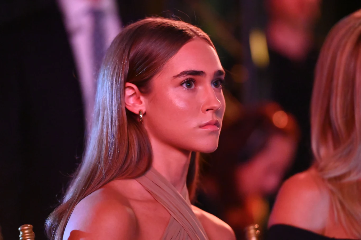 Anastazja Kuś Młoda kobieta o długich, prostych włosach siedzi w eleganckim otoczeniu, skupiona i zwrócona lekko w bok, ubrana w jasną sukienkę z odkrytymi ramionami.
