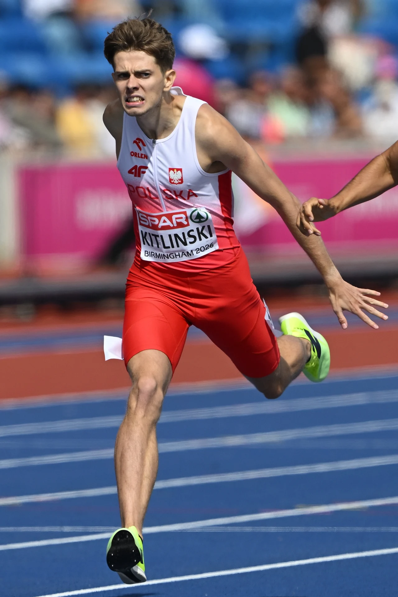 Bartosz Kitliński Polski lekkoatleta w czerwono-białym stroju energicznie finiszujący na bieżni podczas zawodów sportowych, z wyrazem determinacji na twarzy i dynamicznie uniesionymi ramionami.