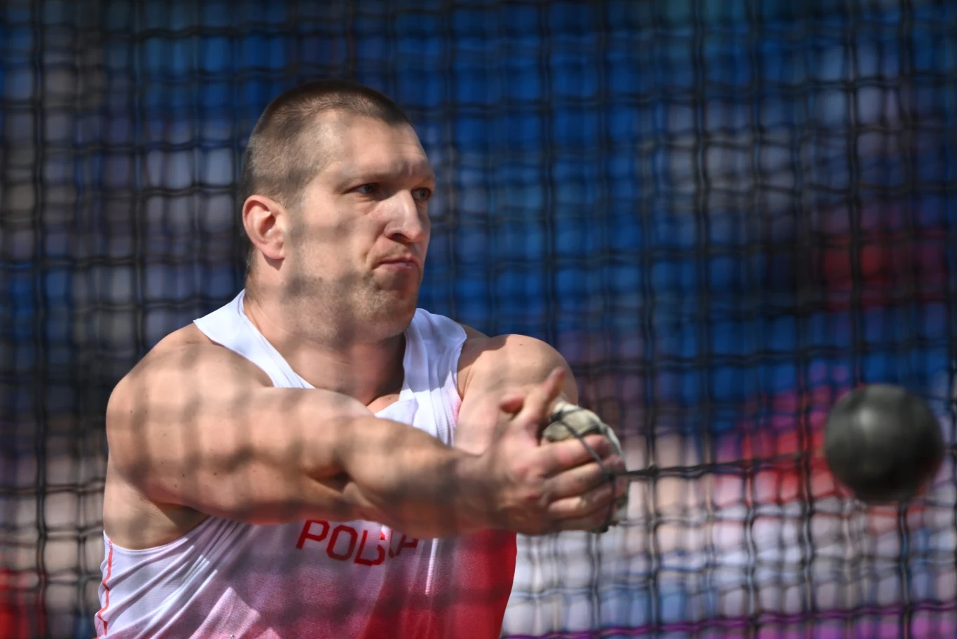 Wojciech Nowicki, Birmingham 2026 Zawodnik w białym stroju sportowym z napisem 'Polska' w trakcie rzutu młotem, z wyrazem skupienia na twarzy, podczas zawodów lekkoatletycznych.