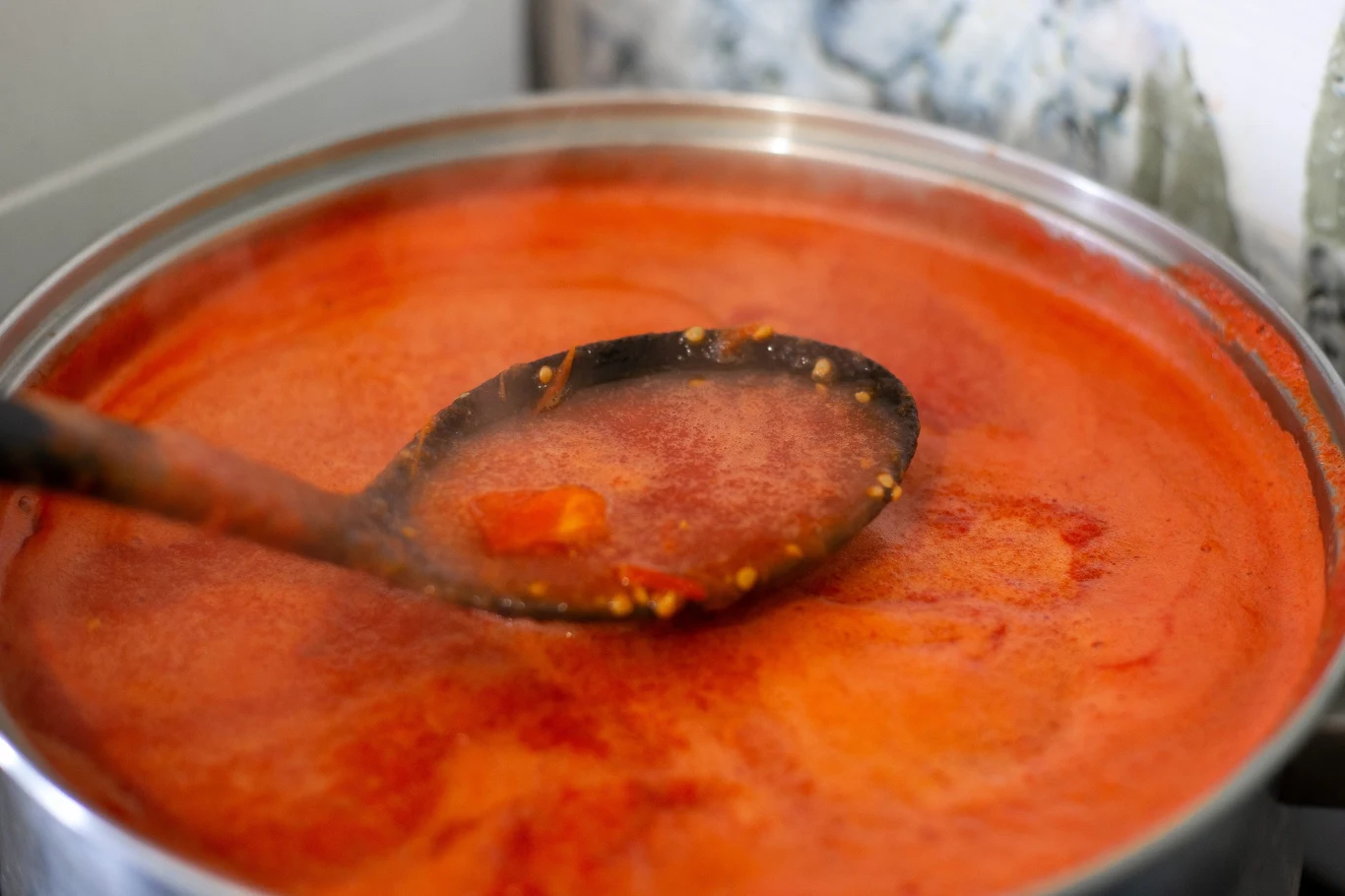 Zupa pomidorowa. Zupa pomidorowa w dużym garnku, czerwony sos pomidorowy z kawałkami warzyw, mieszany czarną chochlą.