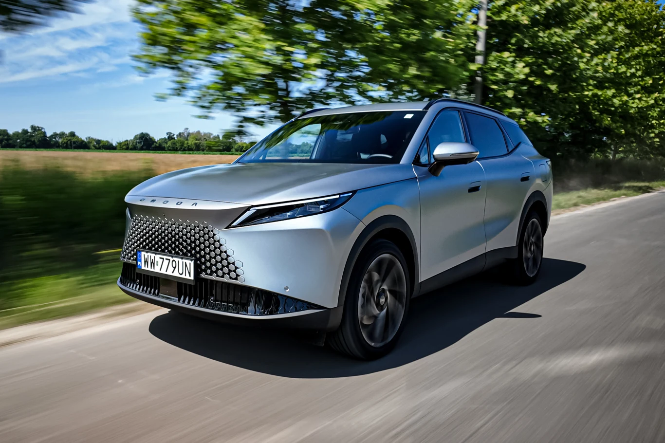 Omoda 7 Super Hybrid to trzeci już model tego chińskiego producenta na polskim rynku Omoda 7 Super Hybrid, srebrny SUV, widok z przodu podczas jazdy po asfaltowej drodze wśród zieleni