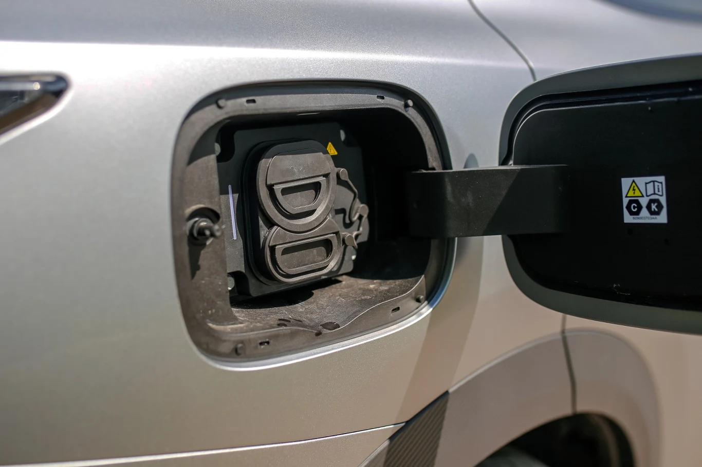 Omodę 7 można ładować prądem stałym o mocy do 40 kW Gniazdo ładowania samochodu elektrycznego z otwartą klapką i widocznymi symbolami ostrzegawczymi.