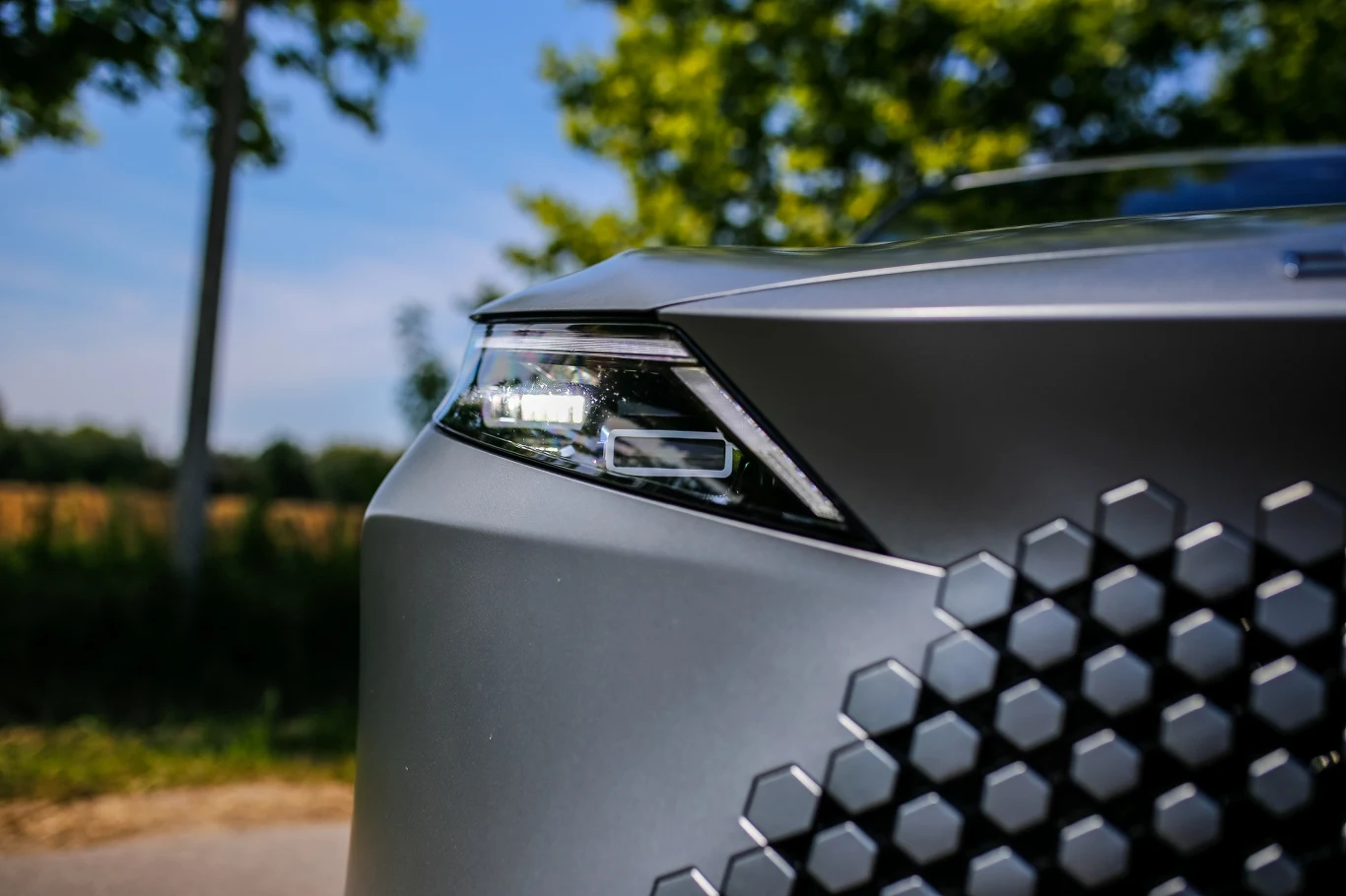 Omoda 7 Super Hybrid Nowoczesny reflektor samochodowy z wyrazistą, geometryczną atrapą chłodnicy o matowym wykończeniu.