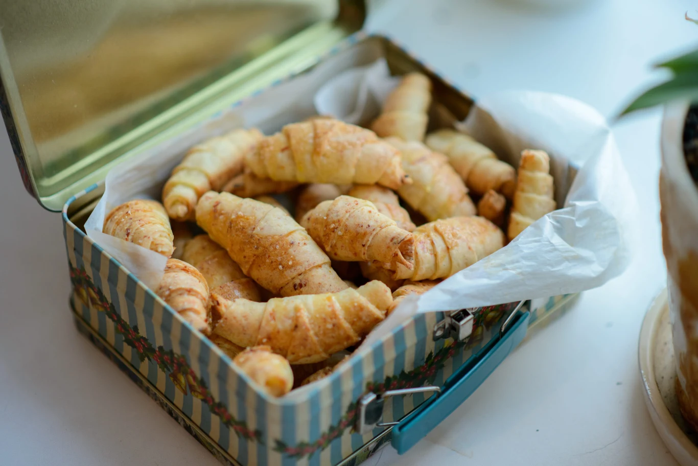 Tradycyjne rugelach idealnie nadają się do popołudniowej kawy Blaszane pudełko wyłożone papierem, wypełnione złocistymi, posypanymi cukrem rugelach.