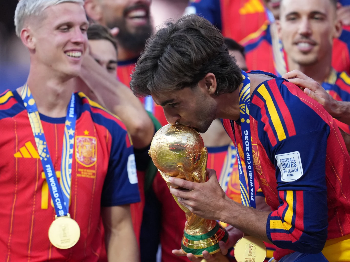 Ferran Torres z pucharem świata Ferran Torres całuje trofeum mistrzostw świata, otoczony przez innych zawodników drużyny świętujących zwycięstwo.
