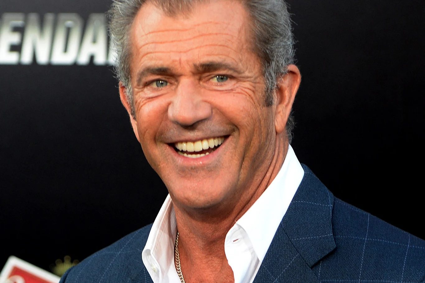 Mel Gibson Mel Gibson w niebieskiej marynarce i białej koszuli pozuje na tle ciemnego, rozmytego tła.