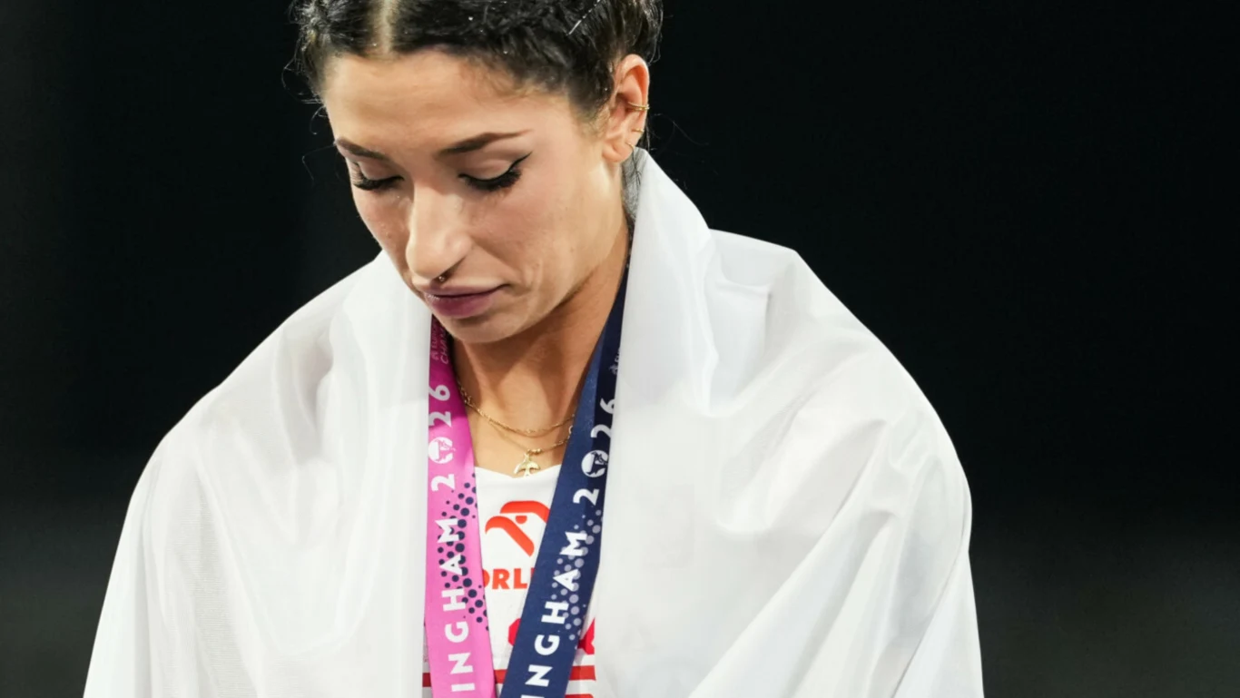 Ewa Swoboda Kobieta z medalem sportowym na szyi, okryta białą flagą, patrząca w dół z poważnym wyrazem twarzy.