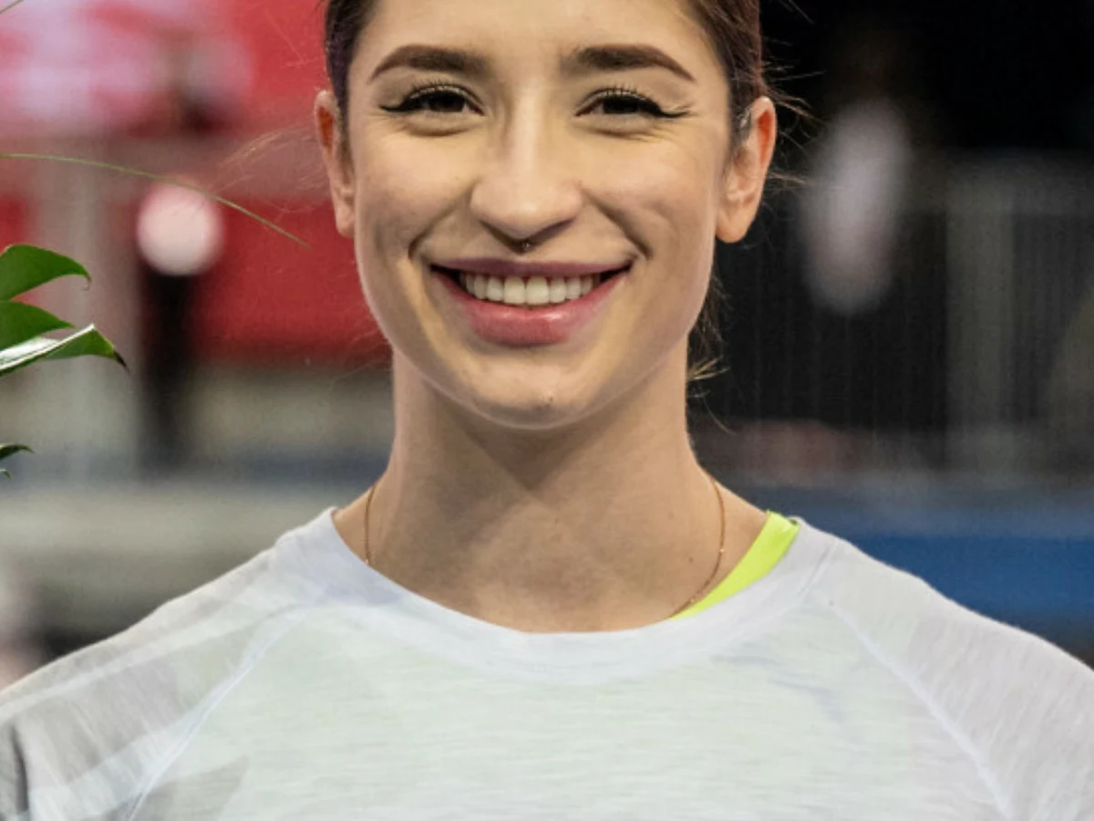 Ewa Swoboda Uśmiechnięta młoda kobieta w białej koszulce sportowej na tle rozmytego wnętrza hali.