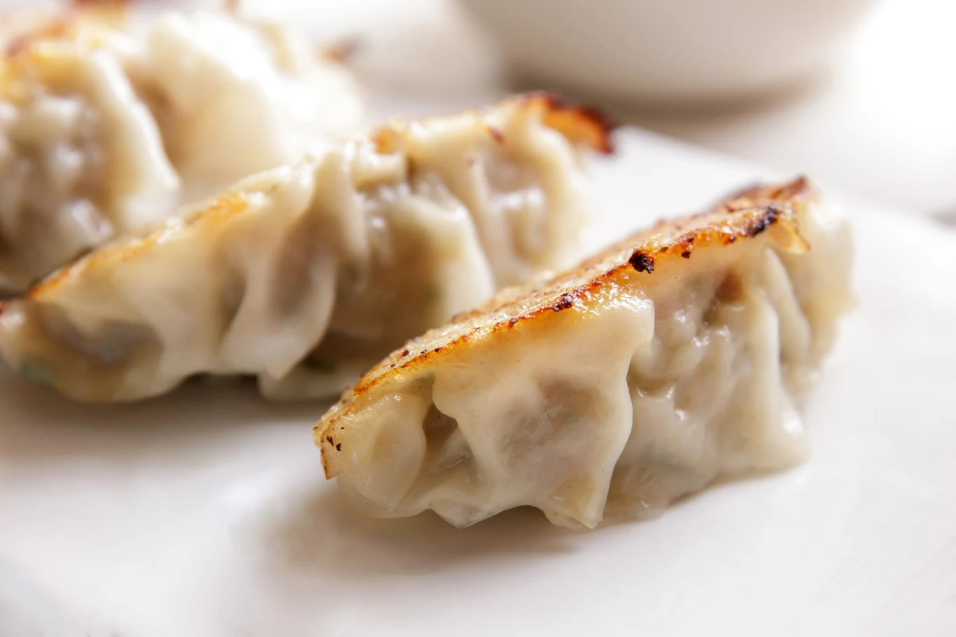 Pierogi z kimchi to wyjątkowy przysmak pochodzący z kuchni koreańskiej Trzy pierogi z kimchi z chrupiącą skórką, ułożone na białym talerzu.