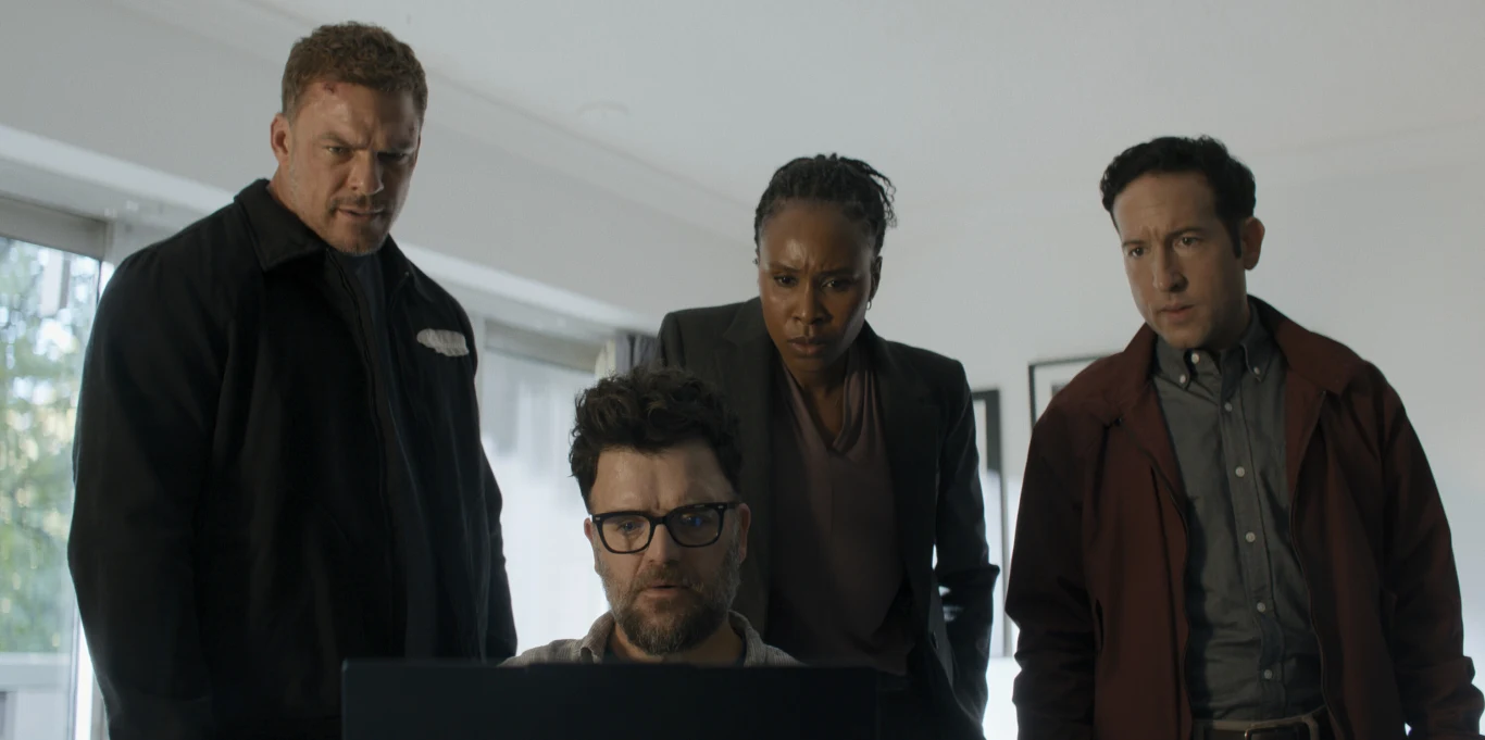 Kadr z czwartego sezonu serialu "Reacher" Cztery osoby stojące i siedzące skupione wokół laptopa, wpatrzone w ekran z powagą i zainteresowaniem.