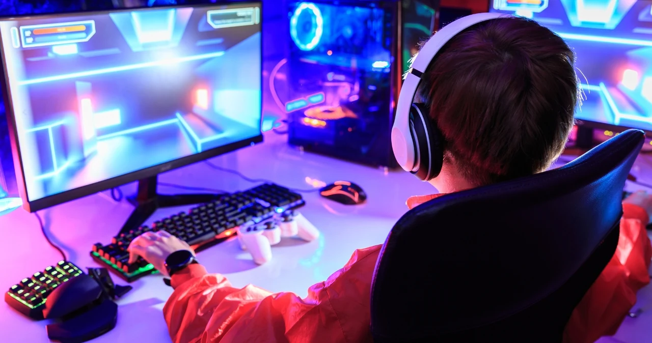 Gamingowe gadżety od 24,99 zł w E.Leclerc. Nie tylko gracze będą nimi zainteresowani Chłopiec w słuchawkach przy komputerze z podświetlaną klawiaturą i sprzętem gamingowym w świetle LED.