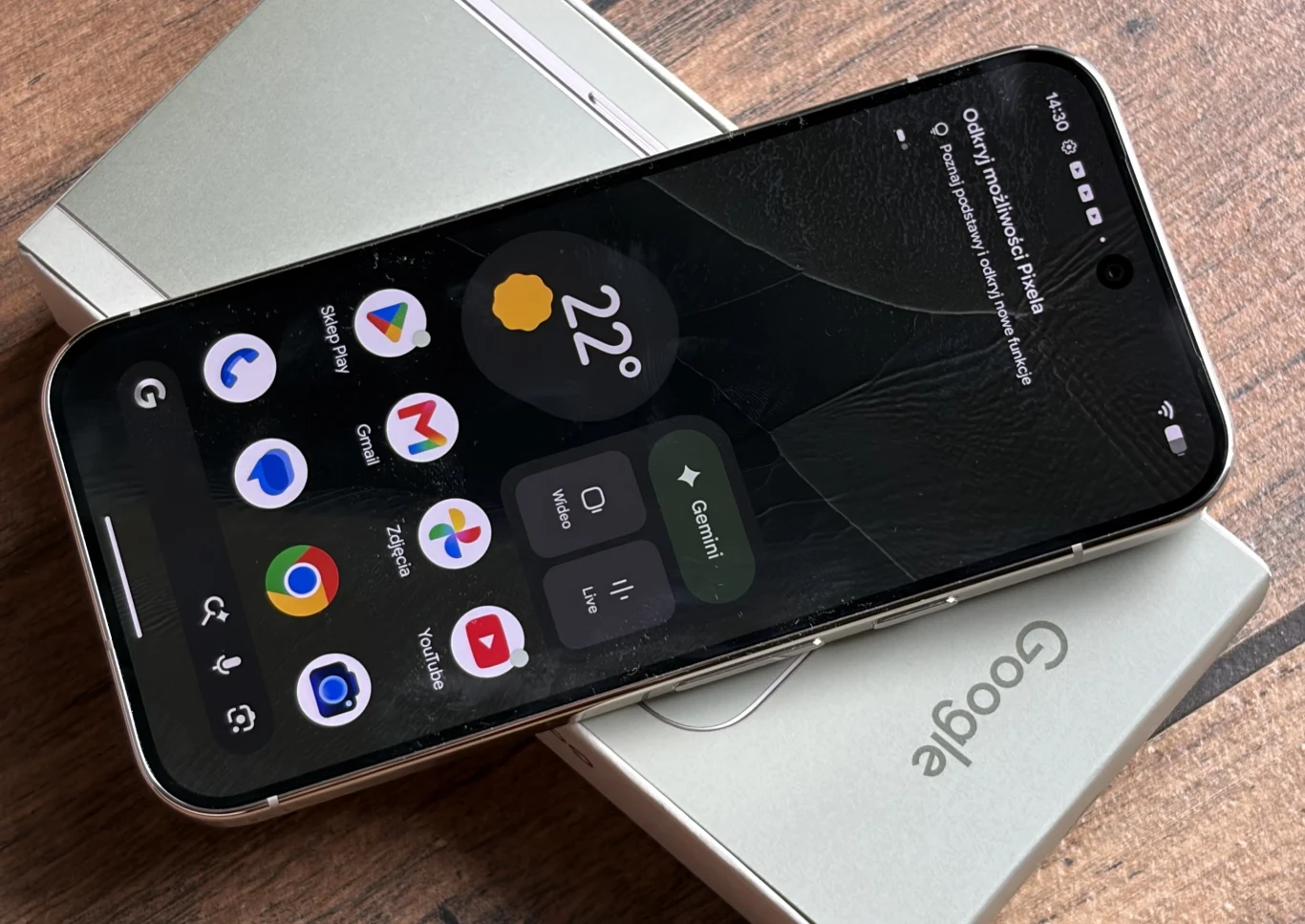Smartfony Google Pixel 11 mają ekrany AMOLED-owe Actua. Smartfon Google Pixel z widocznym pęknięciem na ekranie, leżący na oryginalnym pudełku na drewnianej powierzchni.