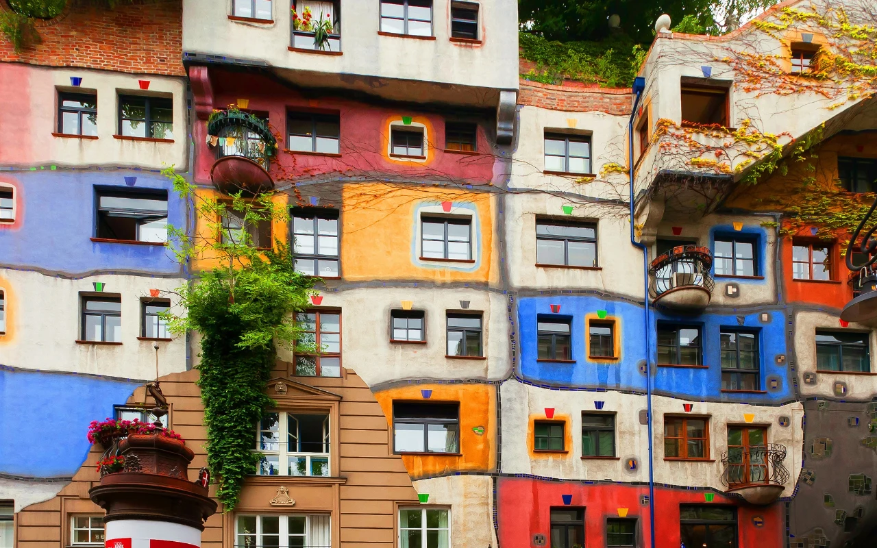 Hundertwasserhaus w Wiedniu Fasada Hundertwasserhaus z patchworkiem wielobarwnych prostokątów, nieregularnymi oknami i licznymi roślinami pnącymi.