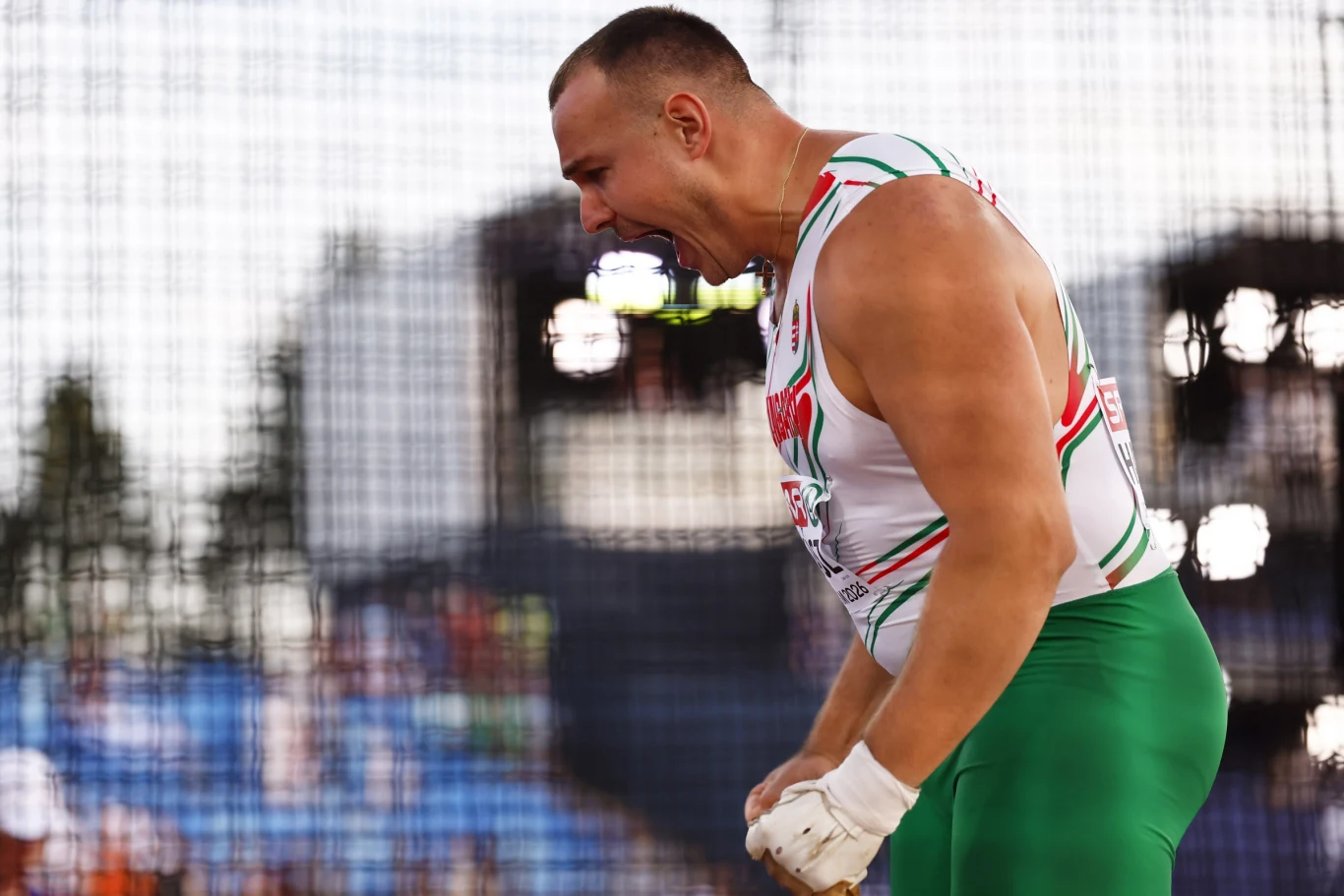 Bence Halasz Zawodnik lekkoatletyczny w emocjonalnej pozie, ubrany w sportowy strój z biało-zielonymi elementami, z zaciśniętymi pięściami, wyrażający ekscytację lub triumf po udanej próbie.