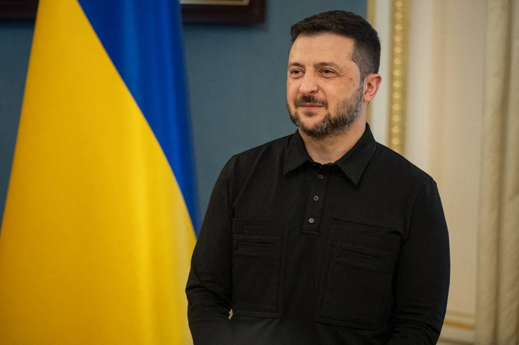 Zełenski: Ukraina przekazała USA propozycje na rozmowy pokojowe z Rosją Wołodymyr Zełenski w czarnej koszuli stoi na tle flagi Ukrainy w eleganckim wnętrzu.